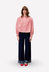 Rood en witte gestreepte cropped blouse met pofmouwen en knopen aan de voorkant. Donkerblauwe wijde jeans met denim manchetten en rode schoenen.