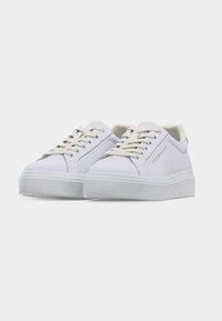 Paire de baskets blanches à plateforme avec des lacets crème et le branding "Tommy Hilfiger" sur le côté, sur un fond gris clair.