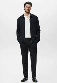 Black jacket with a collared neckline, white polo shirt, and black trousers. Smooth fabric texture with a fitted design. Black ankle boots.