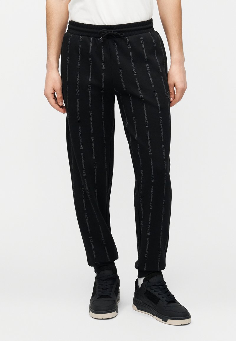 Pantalones jogger negros hechos de material suave, con un ajuste slim y un patrón repetido del logo EAT, cintura elástica y puños en los tobillos.