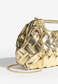 Błyszcząca złota pleciona skórzana torebka z złotym łańcuszkowym paskiem, spoczywająca na białej powierzchni na tle jednolitej bieli.
