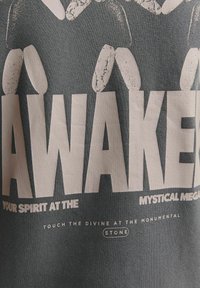 Grå bomulds-T-shirt med fed hvid tekst, der står "AWAKEN" og mindre tekst nedenfor, samt et grafisk design med abstrakte former ovenfor.