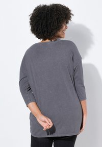 Grijze, langarmige top met een relaxed fit, ronde halslijn en verlaagde schouders. Zacht materiaal met een licht verbleekte textuur.