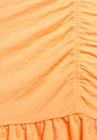 Zmačkaná oranžová látka ukazující jemnou texturu, se shromážděnými švy na jedné straně. Měkký bavlněný materiál s hladkým povrchem.