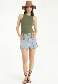 Olivově zelený žebrovaný top bez rukávů, světle modrá džínová plisovaná mini sukně a černé sandály na pásky. Letní klobouk dotváří outfit.