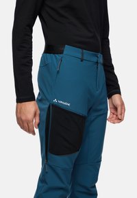 Blauwe outdoorbroeken met een gestructureerde zwarte zak, verstelbare tailleband en een ritszak aan de zijkant. Gemaakt van duurzaam materiaal.