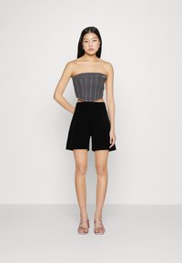 Grå denimtop utan axelremmar med vertikal sömnad, kombinerad med svarta högmidjade shorts och rosa klacksandaler. En enkel, modern design.