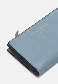 Portafogli in pelle azzurro chiaro con superficie texturizzata, interno nero e logo embossato argentato, caratterizzato da pieghe strutturate e chiusura con zip.