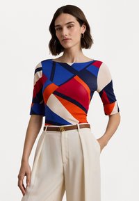 Top de estampado geométrico colorido con mangas cortas, que presenta patrones en azul, rojo, naranja y beige. Complementado con un cinturón marrón.