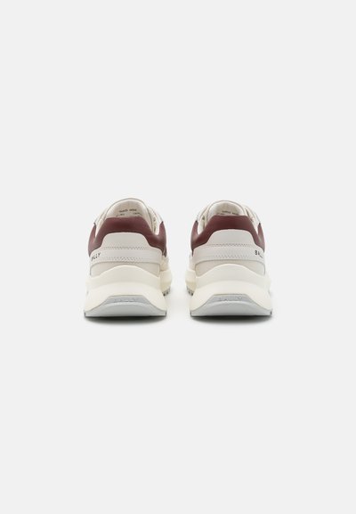 Αθλητικά παπούτσια με κρέμα επάνω μέρος, μπορντό λεπτομέρειες στη φτέρνα και υφή στη μύτη. Περιλαμβάνει επωνυμία και σχέδιο στρωματοποιημένης σόλας.