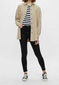 Beige rutig skjorta med knäppning över en marinblå och vit randig topp, kombinerad med svarta skinny jeans och svarta sneakers.