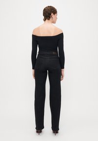 Fekete, vállnál kivágott, hosszú ujjú felső, magas derekú, fekete farmernadrággal, egyenes szabással. Hátsó zsebekkel és minimális részletezéssel rendelkezik.