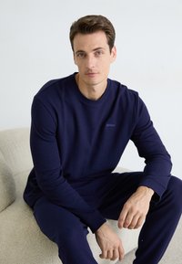 Navyblaue Waffle-Strick-Sweatshirt mit Rundhalsausschnitt und langen Ärmeln; verfügt über kleines 'HUGO'-Logo auf der Brust; kombiniert mit passenden Hosen.