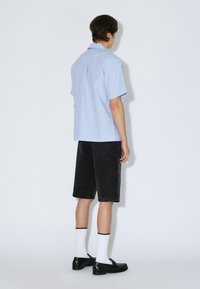 Sinivalkoraidallinen lyhythihainen paita yhdistettynä mustiin farkkushortseihin, valkoisiin sukkiin ja mustiin kenkiin. Takakuvassa korostuu rento istuvuus.