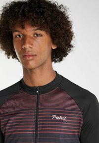 Černý zip-up rash guard s vínovo-černým pruhovaným vzorem a logem na hrudi. Vyrobeno z lehkého, strukturovaného materiálu.