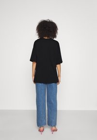 Czarny oversize'owy T-shirt z krótkim rękawem, zestawiony z jasnoniebieskimi dżinsami o szerokich nogawkach oraz różowymi sandałami na wysokim obcasie.