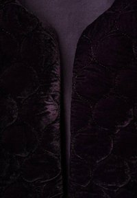 Tessuto in velluto viola scuro con un motivo trapuntato di cerchi, caratterizzato da una superficie liscia e un leggero luccichio, posato su uno sfondo uniforme.