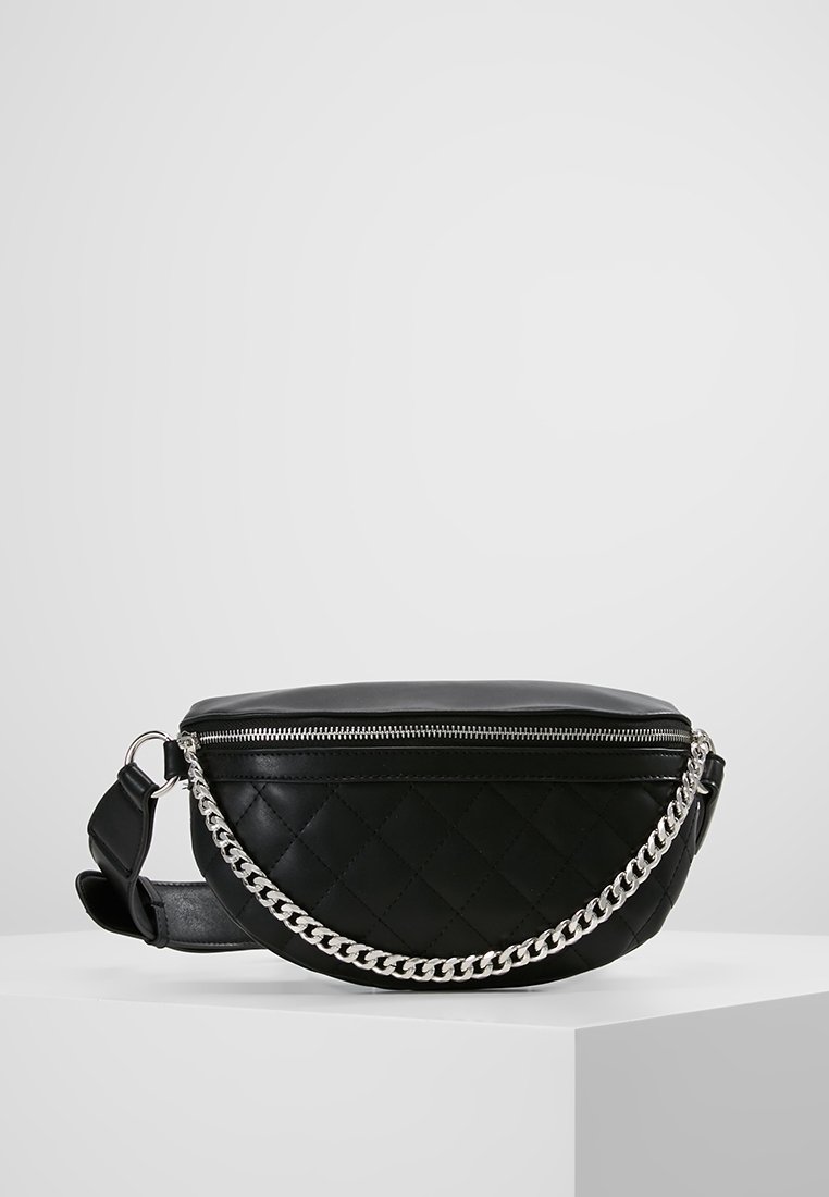 Sac banane en cuir noir matelassé avec fermeture éclair argentée et détail chaîne argentée sur une surface blanche unie.