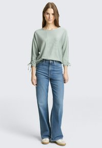 Svijetlozeleni top dugih rukava s rebrastom teksturom, uparen s visokim strukom i izrezanim plavim trapericama. Ležeran izgled upotpunjen mekanom obućom.