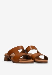 Sandalias de cuero marrón con dos amplias correas cruzadas y un pequeño tacón cuadrado. Textura suave con detalles recortados, montadas sobre una suela que simula madera.