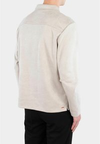 Ljusbeige långärmad skjorta med mjuk-textur, kragdetsign och detalj på baksemen. Liten orange accent vid fållen.