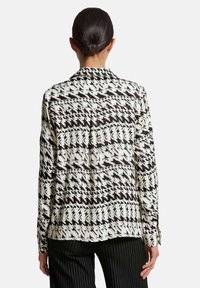 Langarmshirt mit einem schwarz-weißen Hahnentrittmuster, glatter Textur und klassischem Kragen, kombiniert mit gestreiften Hosen.