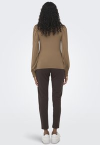 Top marrón de manga larga con hombros abullonados, combinado con pantalones tapered marrón oscuro y zapatillas blancas. Textura suave, diseño ajustado.