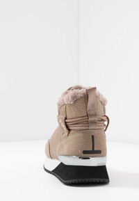Zapatillas de invierno beige con forro de piel, tiro de tela, cordones envolventes, talón de gamuza texturizada y suela de goma negra con detalles en blanco y plata.