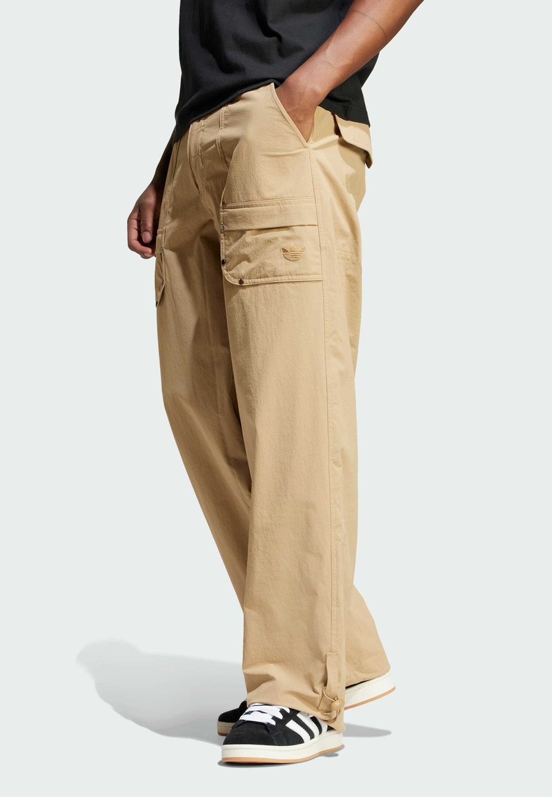 Pantaloni cargo beige, morbidi e larghi, con molteplici tasche e chiusure a scatto. Realizzati in materiale leggero, abbinati a sneakers bianche e nere.
