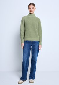 Gebreide, coltrui in zacht groen. Gekocht met blauwe rechte jeans en lichtgekleurde sneakers. Eenvoudig, gestructureerd ontwerp.