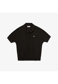 Svart polo t-shirt med korta ärmar, krage och ribbad nederkant, med en liten grön Lacoste krokodil-logotyp på bröstet. Materialet är bomull.
