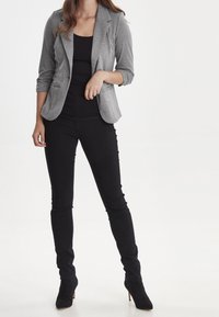 Gray blazer made of textured fabric, paired with a black top and fitted black pants. Footwear is black suede boots with a pointed toe.