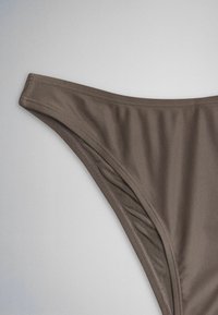Brauner Bikinihöschen mit genähten Kanten auf hellgrauem Hintergrund, zeigt glattes Gewebe und schlichtes Design.