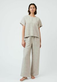 Ensemble en deux pièces beige clair fait de tissu texturé. Le haut a des manches courtes et une coupe décontractée ; le pantalon possède une jambe large et une taille avec cordon.