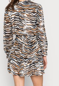 Robe transparente à étages en noir, blanc et rayures orange de tigre ; dotée de manches longues et d'une taille élastique pour un ajustement réglable.