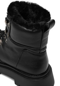 Czarne skórzane buty z sztucznym futrem w kołnierzu, zaokrąglony fason, wyraźne przeszycia i szczegółowe akcenty metalowe dla pewnego sznurowania.