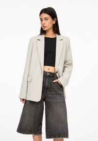Hellgraues Blazer mit Revers, einem Knopfverschluss und seitlichen Taschen, kombiniert mit hochtaillierten schwarzen Denim-Culottes mit fransigem Saum.