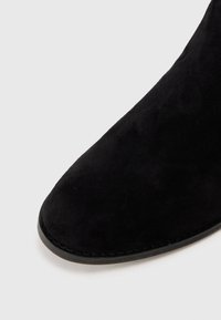 Fekete velúr bokacsizma kerek orral és varrott szélekkel, sima felülettel és minimalista dizájnnal.