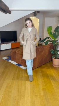 Manteau beige avec une ceinture et un col à revers, porté sur un haut blanc et un jean bleu clair. Texture douce, associé à des bottines marron.