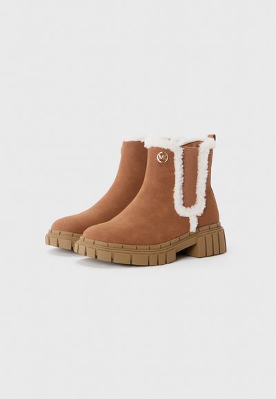 Botas ankle em camurça castanha com um colar de pêlo branco suave, sola de borracha e painéis elásticos laterais para facilitar o calçar. Apresentam um detalhe de logo prateado.