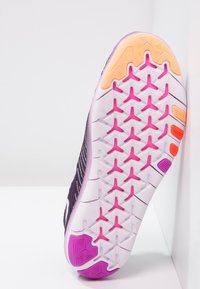 Violetti urheilukengän pohja, jossa on pinkki ja oranssi pito kuvio, teksturoitu pinta ja valkoinen Nike-logo.