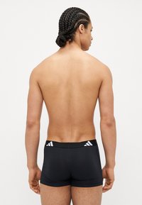 Shorts deportivos negros con un diseño ajustado, que presentan una cinturilla ancha con acentos de tres rayas blancas. Textura suave, de longitud media.