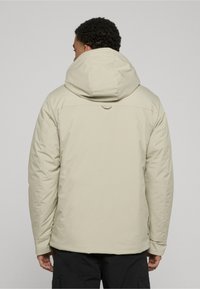 Light beige puffer jacket with a fitted hood, visible stitching, and a smooth texture. Features a tab at the neck for adjustment.