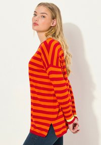 Röd och orange randig långärmad topp med sidsprund och avslappnad passform. Tillverkad av mjukt tyg med kontrasterande ärmslut.