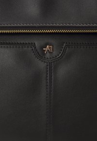 Černá kožená taška se zlatými kovovými prvky, se středním zipovým uzávěrem a embosovaným logem. Hladký povrch s jemným prošíváním.