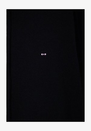 Tissu tricoté noir avec un petit logo rose brodé, centré, représentant deux yeux stylisés.