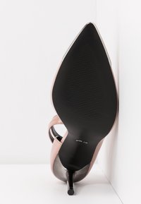 Chaussure à talons hauts rose avec bout pointu et semelle noire texturée. Elle présente un talon brillant et des brides à design ouvert.