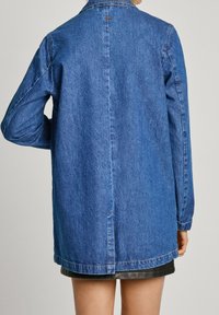 Modrá džínová bunda s límečkem, dlouhými rukávy a rovný střih. Má výrazné švy a boční rozparek na lem.