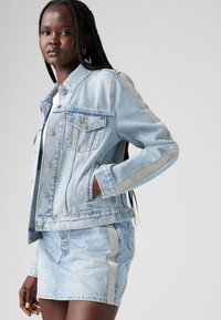 Giacca di jeans blu chiaro con dettagli argentati e una gonna abbinata. Presenta uno stile classico, tasche frontali e un colletto. Tessuto texturizzato.