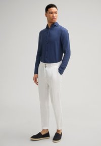 Navyblaue Leinenhemd mit langen Ärmeln und Button-Down-Kragen, kombiniert mit weißen Leinenhosen und schwarzen Espadrilles.